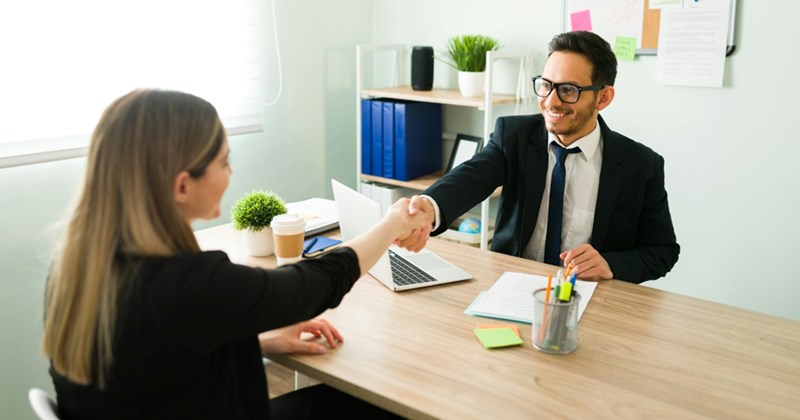 A representation of a male manager and a female employee shaking hands over a desk