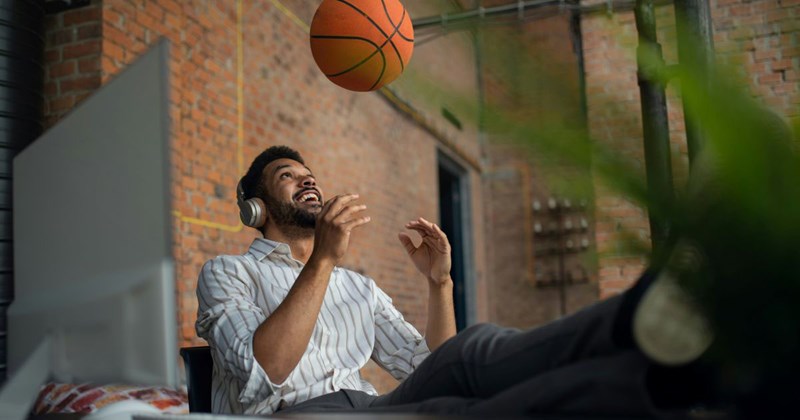 An employee playing with a basketball at his desk to pass the time, doing something that has nothing to do with his actual job