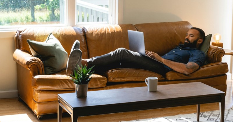 A model representing an employee lying on a couch and working from home on his laptop