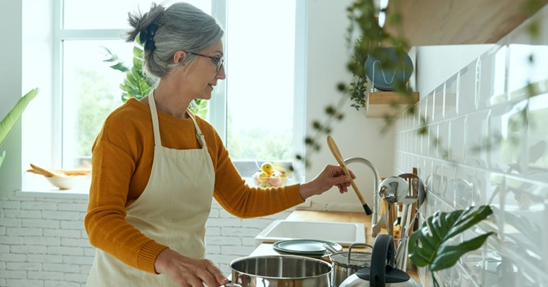 A model representing an older woman picking up a wooden spoon in a kitchen