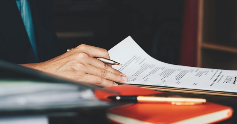 A woman's hand flicking through a resume on a clipboard while holding a pen