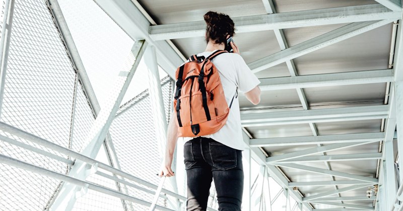 A man walks across an airport bridge, wearing a backpack