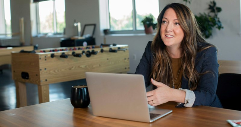 A manager discusses something as she sits behind a laptop with a mug by the side