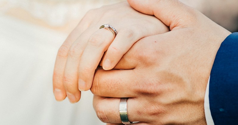 A close-up of a man holding a woman's hand, with both wearing wedding/engagement rings