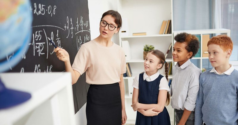 An Elementary school teacher instructs her students in math on the blackboard before they do their classwork with pencils and paper.