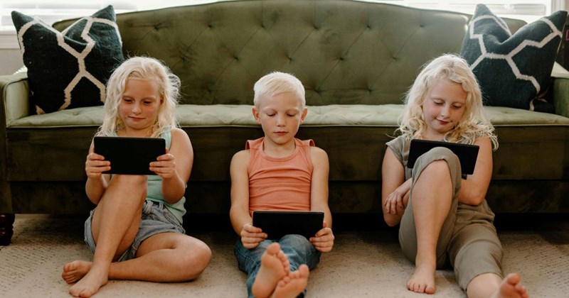 Three young kids are playing on their iPads instead of playing with each other.