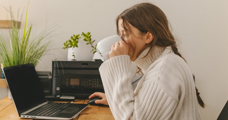 A woman drinks from a mug while working on her laptop at home