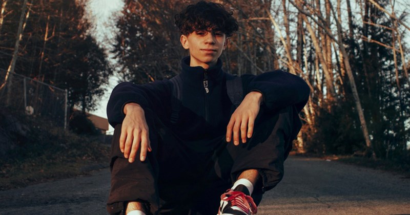 A teenage boy sits in the middle of the road, resting his hands on his legs