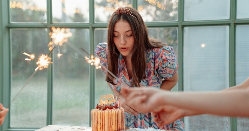 A representation of a woman blowing out the candles on a cake as people hold sparklers over the table in front of her