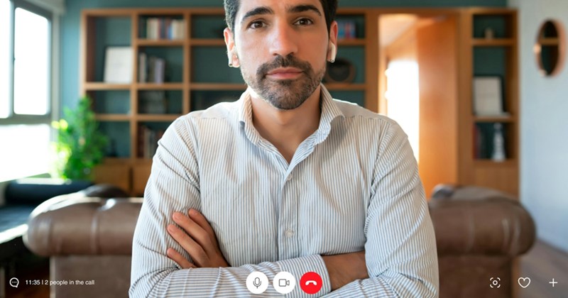A representation of a man sitting on a video call, wearing AirPods with his arms crossed
