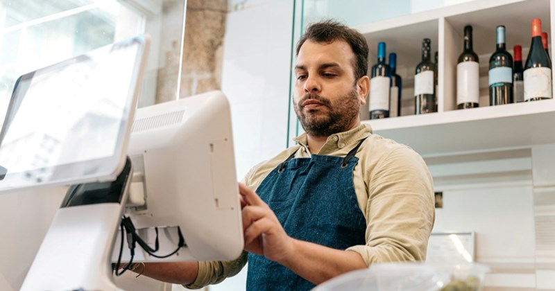 A retail worker wearing a denim apron uses a touch-screen cash register