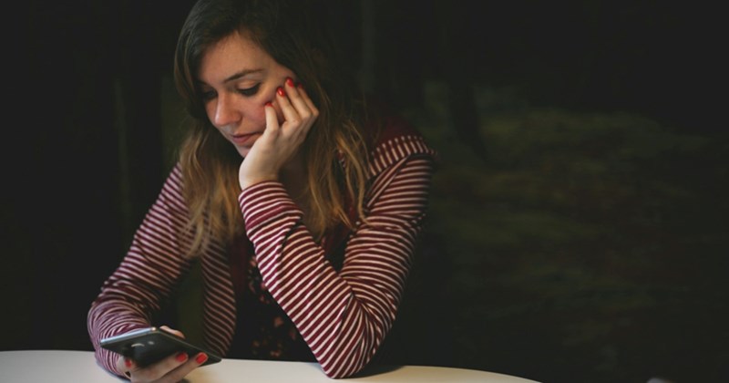 A representation of a woman in a striped shirt sitting and looking at her phone, resting her head in her hand