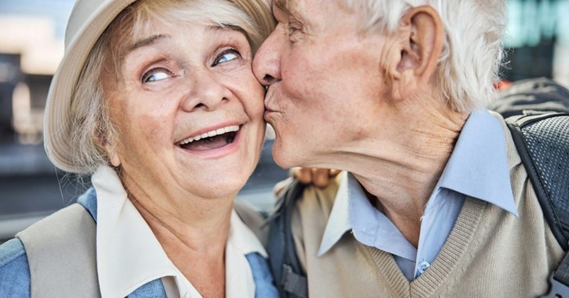 A close-up of an elderly couple on vacation, with the man kissing the woman's cheek