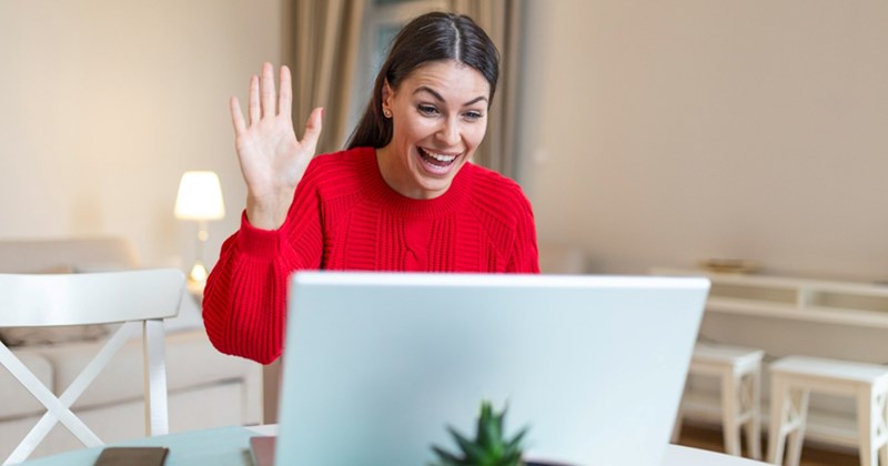 A woman waves while taking a video call from home
