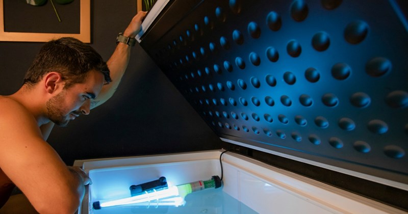 A man looks inside a deep freezer with a blue light inside it