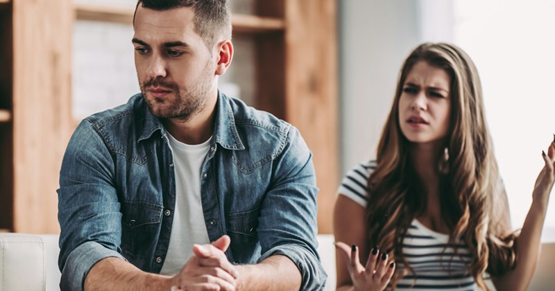 A man looks away from a woman who is berating him as they sit together. 