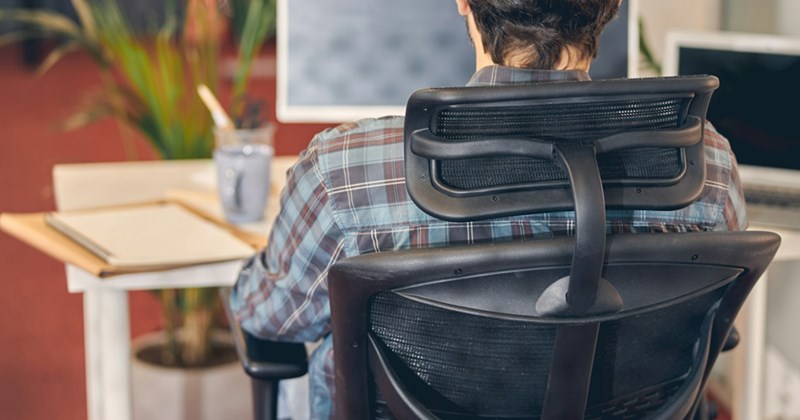 Back view of a male employee sitting at a desk in an office chair. 