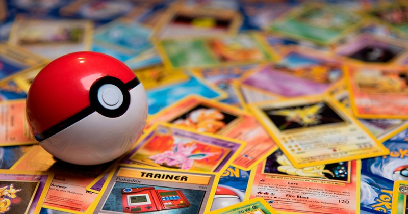 A pile of Pokémon trading cards with a Poké ball sitting on top of them. 