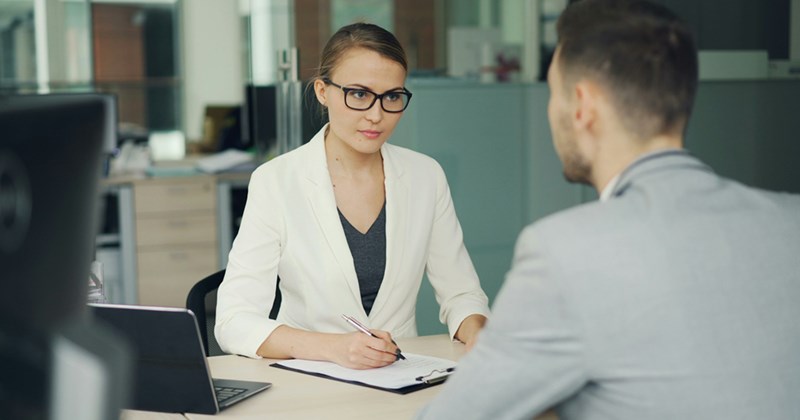A female recruiter sits across the table from a job applicant, interviewing him. 
