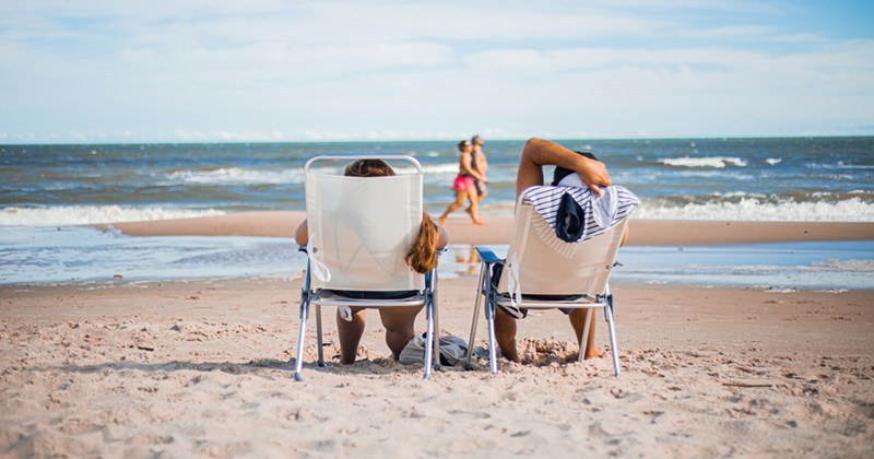 Two people relaxing in folding chairs on the beach, looking at the sea.