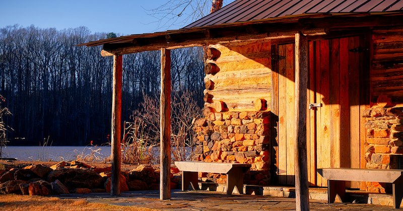 A rustic log cabin next to a body of water. 