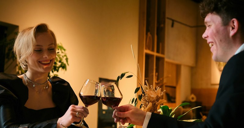 A man and a woman raise a toast with their wine glasses as they sit in a restaurant together.