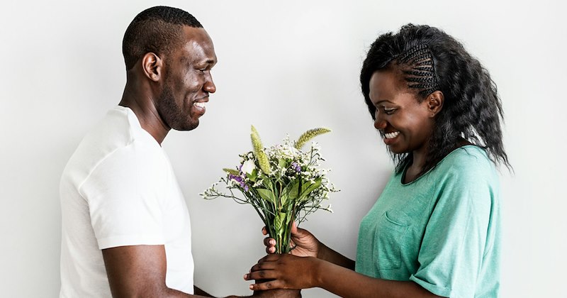 A woman looks happy as her boyfriend gives her a bunch of flowers. 