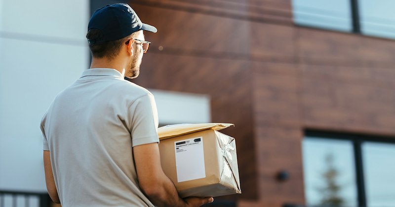 Back view of delivery man carrying parcels for delivery in front of a house.