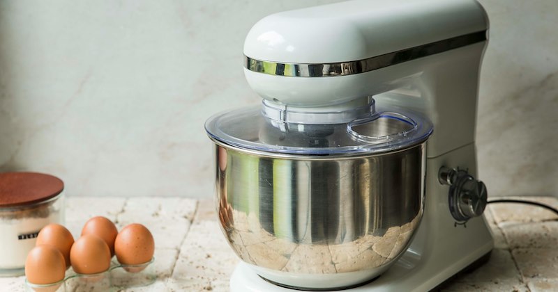 A white stand mixer sitting on a counter next to some eggs.