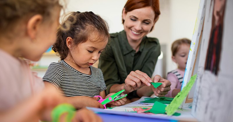 A female daycare assistant helps children do crafts.