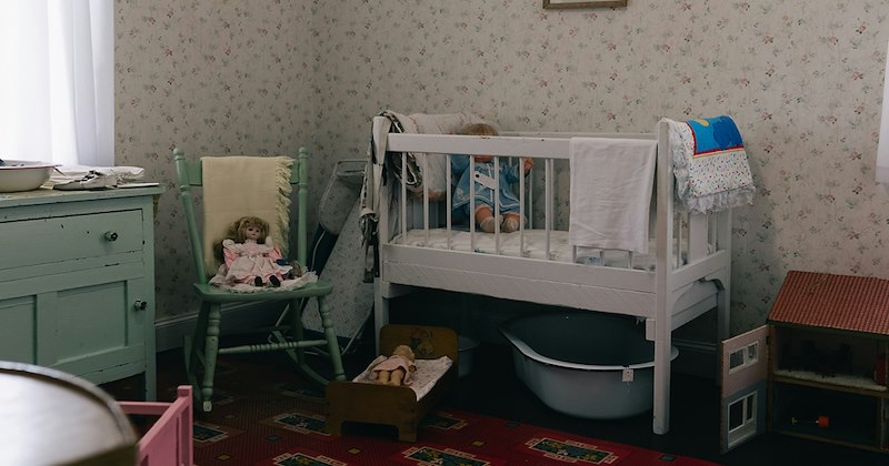 An old-fashioned crib in a wallpapered nursery.