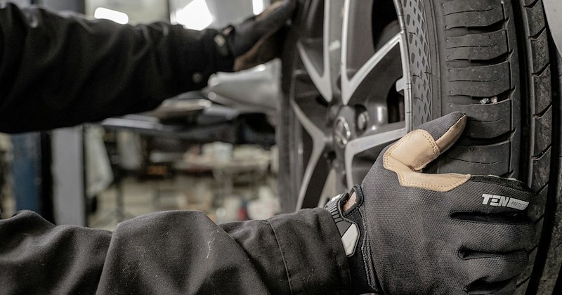Close-up of a mechanic fitting a tire while wearing gloves.