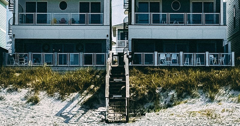Two houses on either side of a staircase leading down to the beach. 