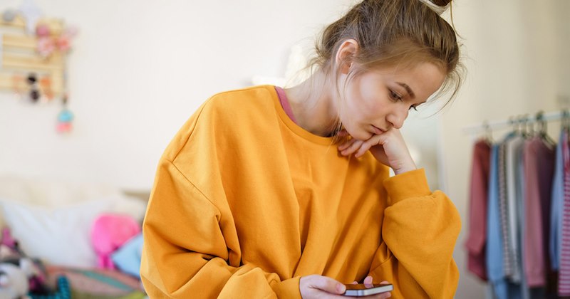 A teenage girl rests her chin on her hand while looking at her phone. 