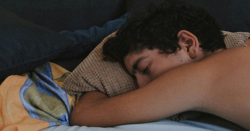 A young man hugs a pillow while sleeping in bed. 